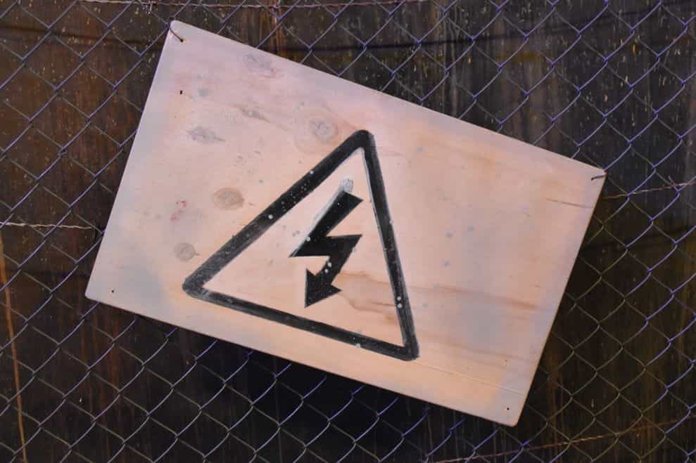 Papan kayu yang diikat ke gerbang menggambarkan tanda peringatan dengan petir di dalamnya.