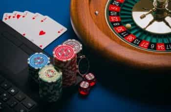 Poker chips, playing cards and a roulette wheel placed close to a laptop.