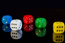 Four die, each one in a different color, laying on a black reflective surface against a black background.