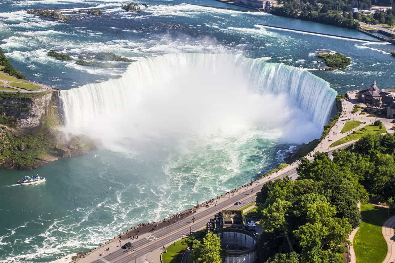 Air terjun Niagara Falls yang ikonis di perbatasan negara bagian New York dan provinsi Ontario di Kanada, dengan kerumunan wisatawan di trotoar di sekitar tengara.