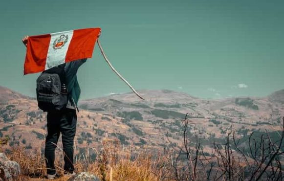 A man carries a Peruvian flag behind his back on a mountain.