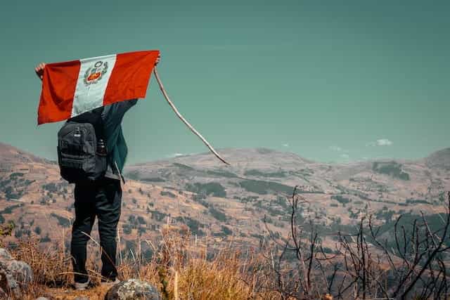 Seorang pria membawa bendera Peru di belakang punggungnya di atas gunung.