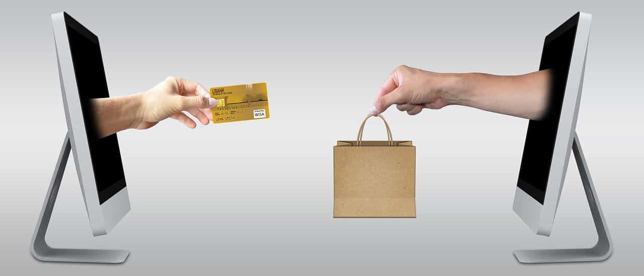 Two computer monitors facing one another, with one hand extending out of one with a credit card, while another featuring a hand holding a paper bag coming out of it.