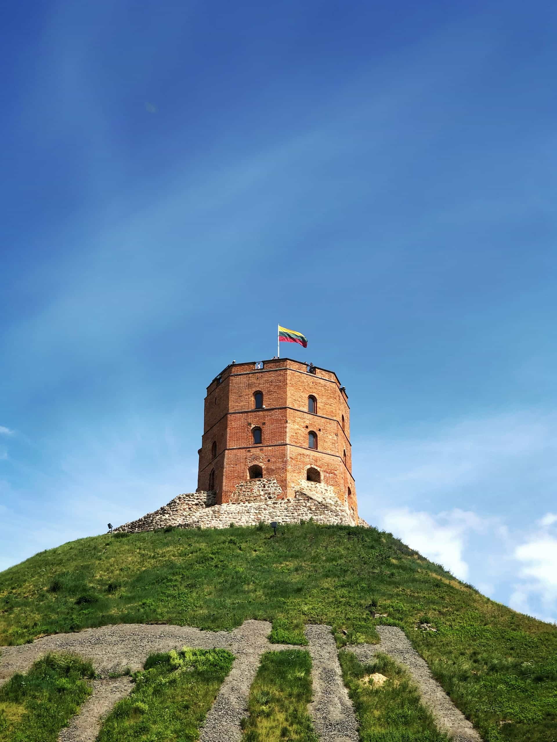 Sebuah bukit dengan kastil di atasnya mengibarkan bendera Lituania. 