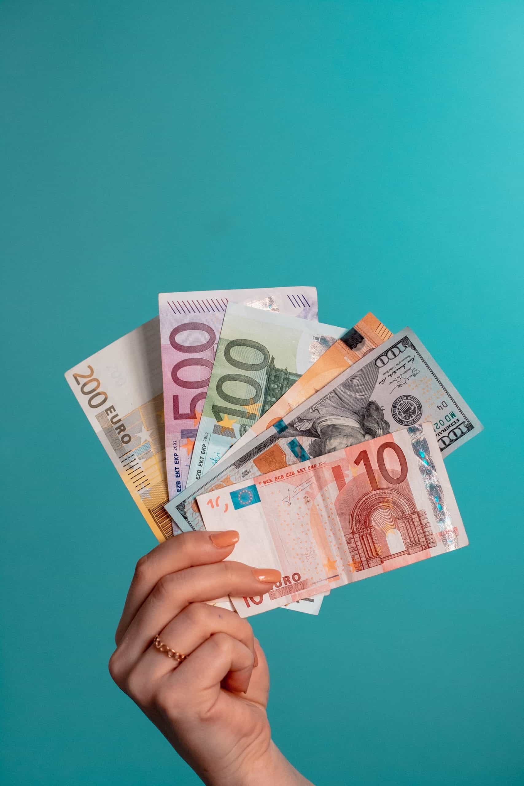 Tangan seorang wanita memegang beberapa denominasi euro.