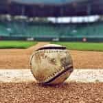 A worn-out baseball sitting in the dirt of a baseball pitch in a baseball stadium before game time.