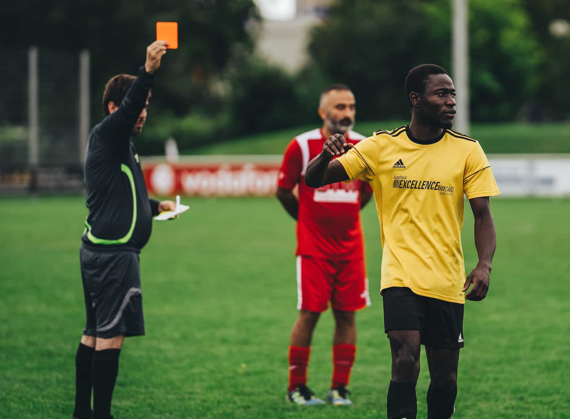 Dua pemain sepak bola dan wasit memegang kartu penalti merah.