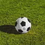 A soccer ball on a bright green grass soccer field.