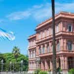 A pink government building, Casa Rosada, in Buenos Aires, with an Argentina flag waving outside on a bright day.