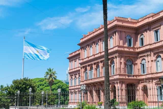 Gedung pemerintah merah muda, Casa Rosada, di Buenos Aires, dengan bendera Argentina berkibar di luar pada hari yang cerah.