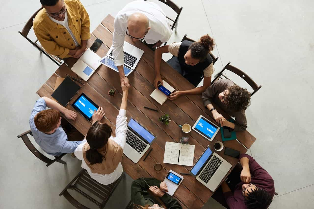 Kolega duduk mengelilingi meja dalam rapat dengan laptop.