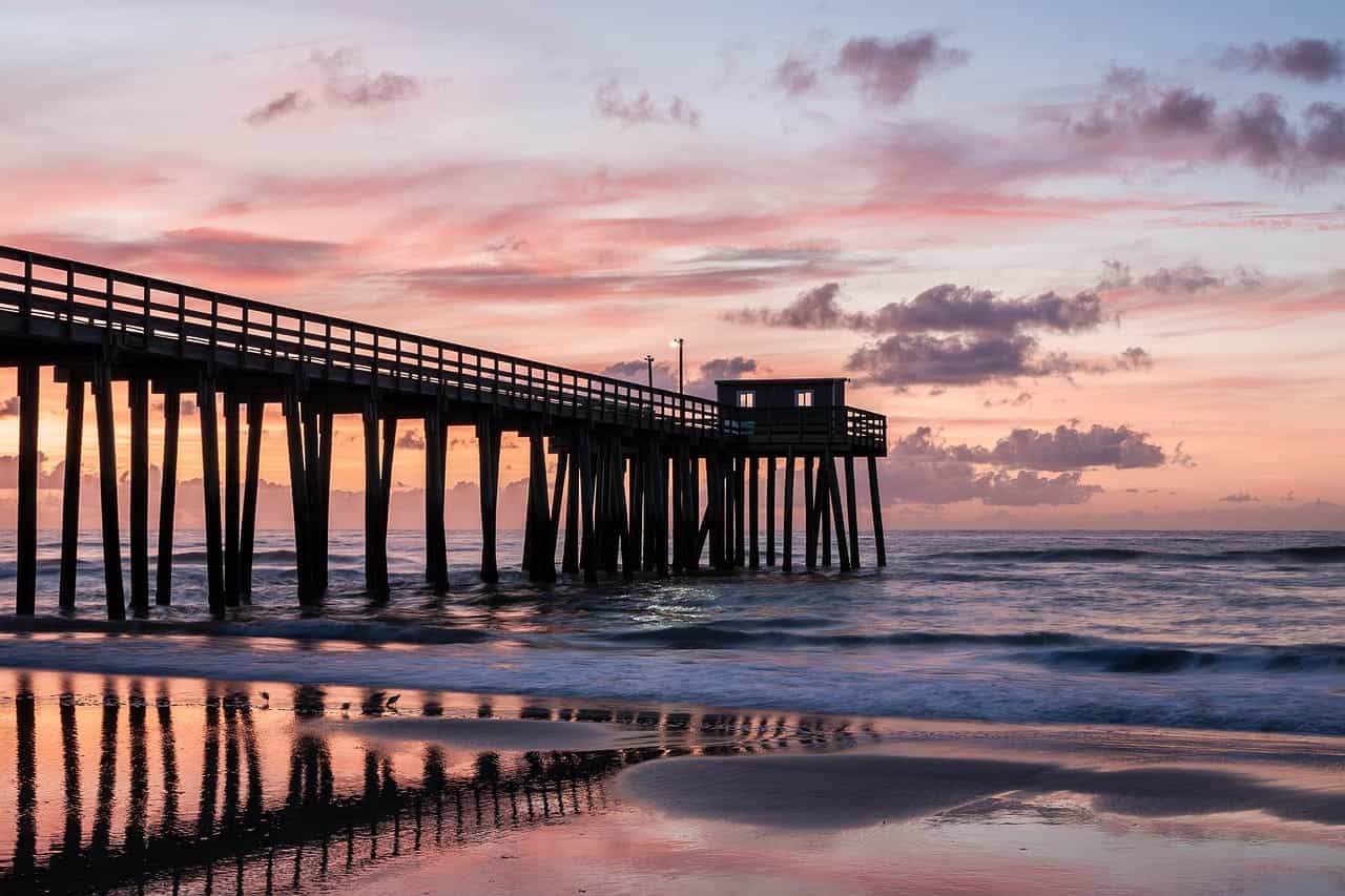 A large wooden jetty extending into the seashore on a beach in New Jersey during sunset.