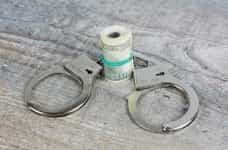 A pair of silver handcuffs sit beside a rolled up wad of cash.