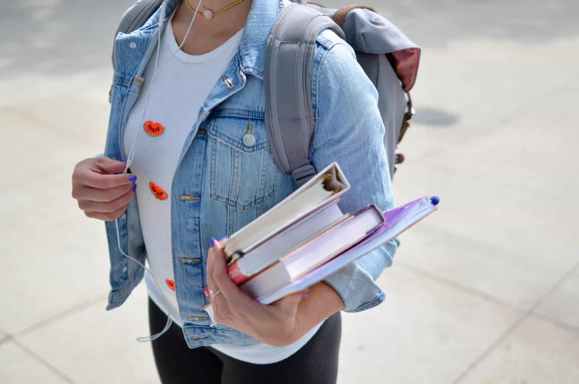 Seorang wanita muda mengenakan ransel memegang buku sekolah.