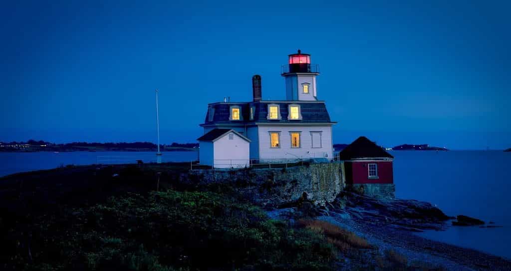 A small lighthouse flanked by a red shack on the small, uninhabited island of Rose Island off the coast of Newport Beach, Rhode Island.