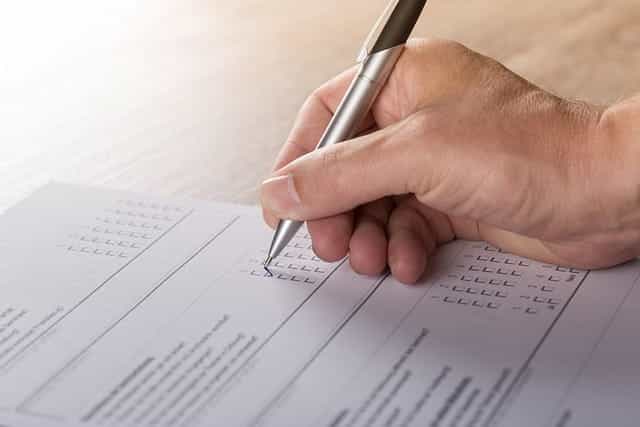 Tangan seseorang mengisi survei pilihan ganda pada formulir di selembar kertas.