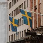 Two flags of Sweden hanging from poles attached to the wall of a building.
