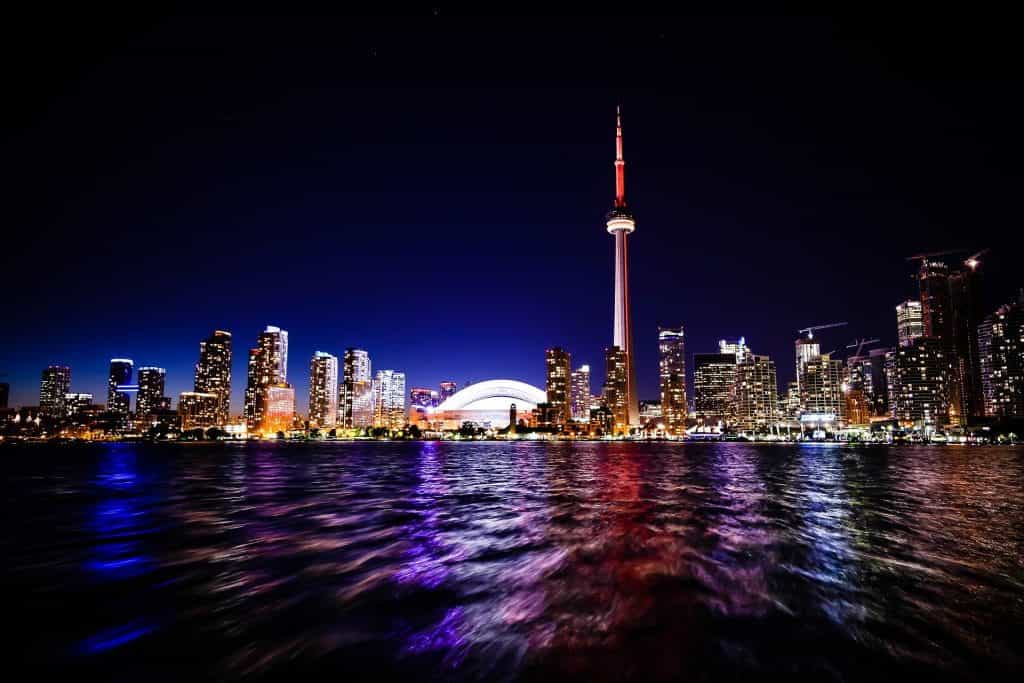 Cakrawala ikonik pusat kota Toronto, Ontario seperti yang terlihat dari perairan Danau Ontario pada malam hari, dengan Menara CN yang terkenal di dunia menjulang di atas gedung pencakar langit dan gedung-gedung tinggi.