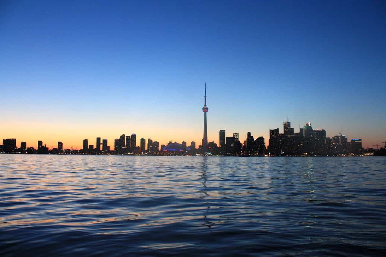 Cakrawala pusat kota Toronto, Ontario di kejauhan terlihat dari perairan Danau Ontario yang terbentang di depannya, dengan Menara CN yang terkenal di dunia di tengahnya. 