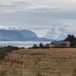 A house in a field on the coast of Puerto Natales, Chile, with snowy mountains in the distance.
