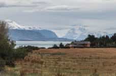 A house in a field on the coast of Puerto Natales, Chile, with snowy mountains in the distance.