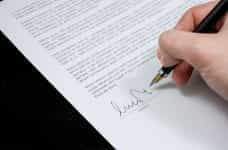 A hand signing a document with a pen.