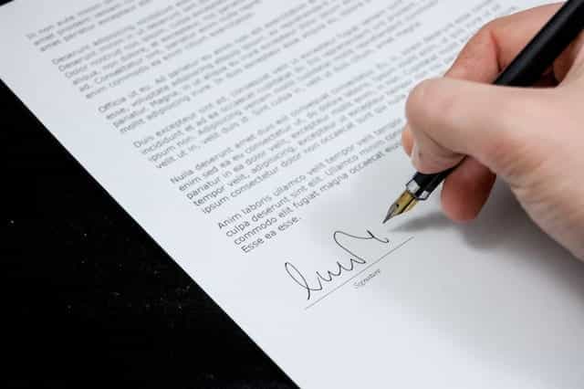 Sebuah tangan menandatangani dokumen dengan pena.
