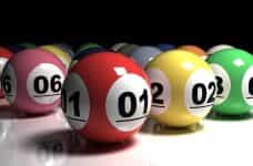 A collection of different colored lottery balls with different numbers on them placed carefully beside one another on a white table surface.