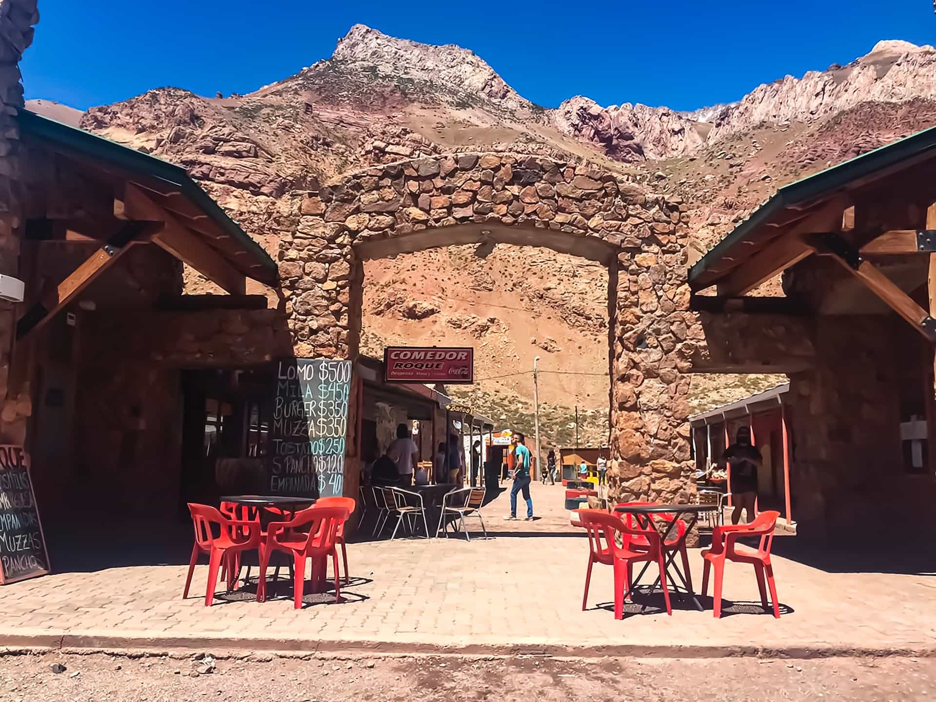 An outdoor cafe with chairs in the midst of a red stone building, in front of red sandy mountains in Mendoza, Argentina.