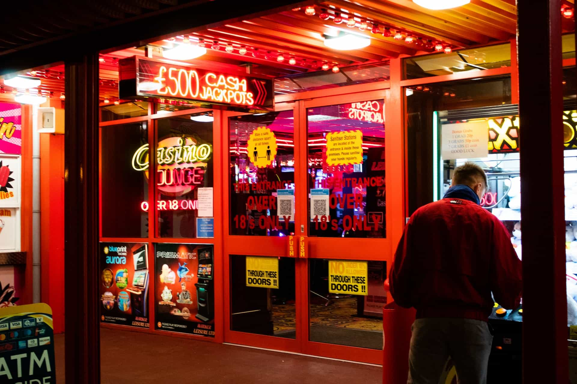 The entrance of a casino with many neon light signs with a reddish glow.