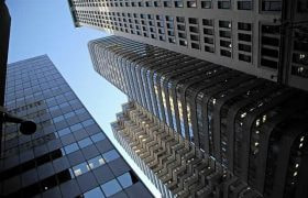 A low-down, ground level shot looking upwards at several tall skyscrapers in the middle of a city’s downtown district.