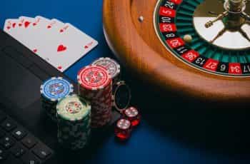A roulette wheel, playing cards, poker chips and dice with a laptop.