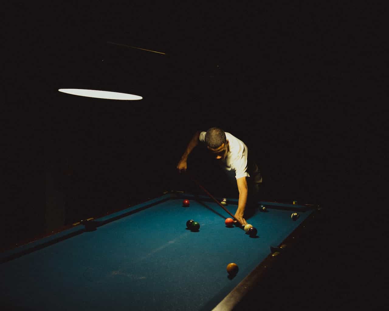 Seorang pria bermain snooker di ruangan gelap.