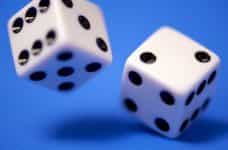 Two white dice spin in front of a blue surface.