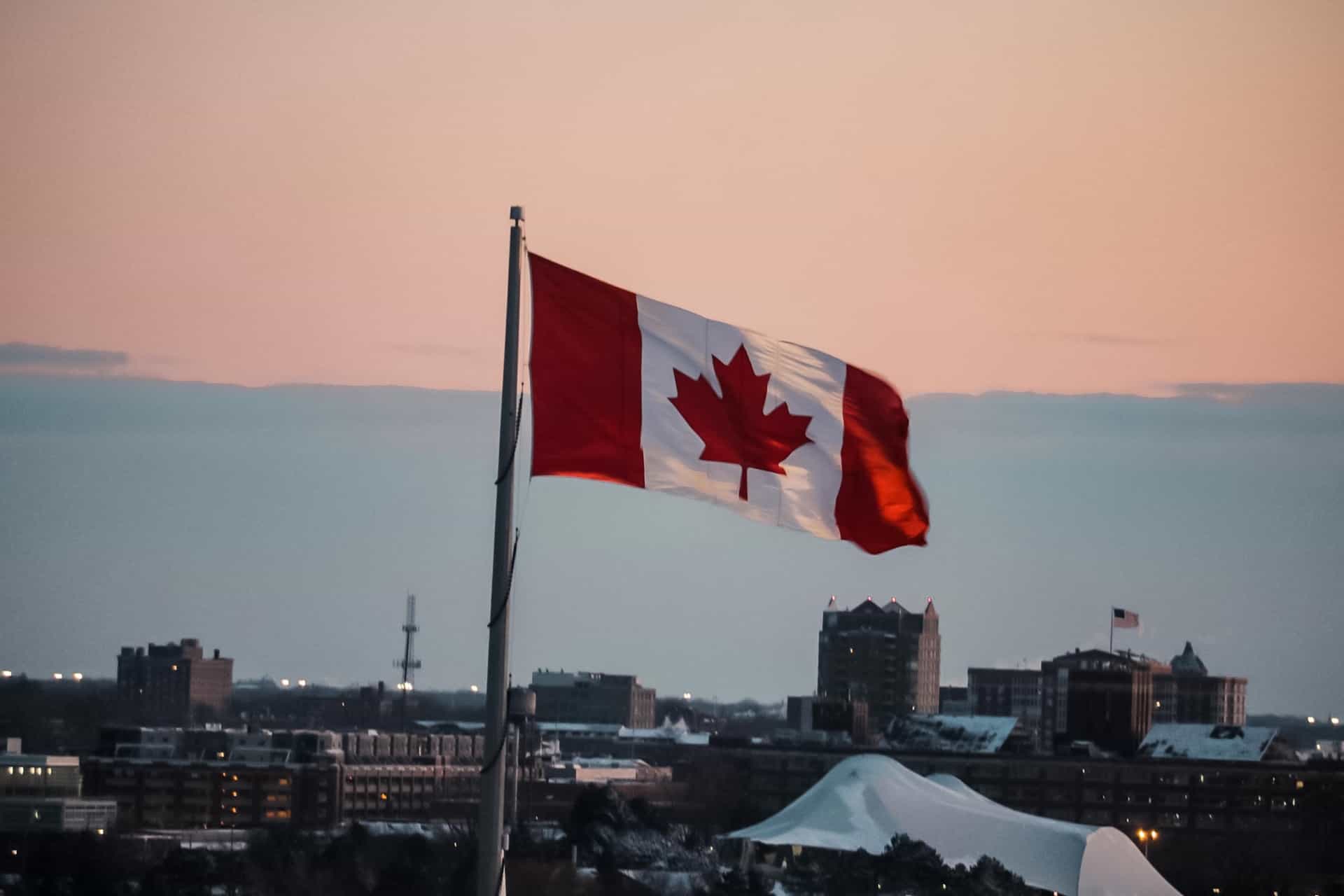 Bendera nasional Kanada, menampilkan warna merah dan putih yang ikonik dan Daun Maple, berkibar tinggi di atas kota di negara tersebut.