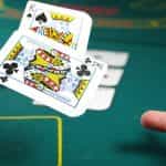 A person’s hand throwing a pair of throwing cards on a casino table during a game of poker.