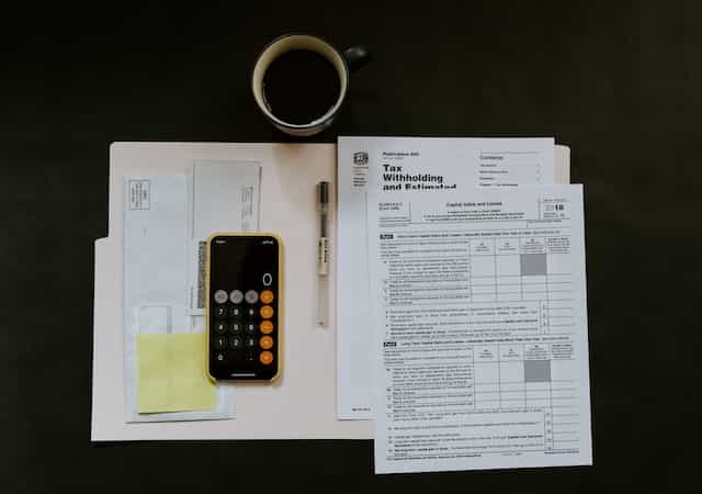 Meja kerja dari atas dengan berbagai dokumen pajak, kalkulator, dan secangkir kopi.