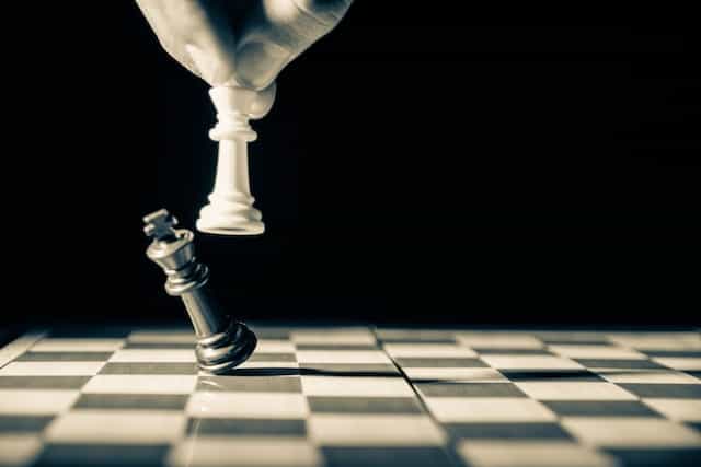 Tangan yang memegang bidak catur putih menjatuhkan bidak catur hitam untuk memenangkan permainan.