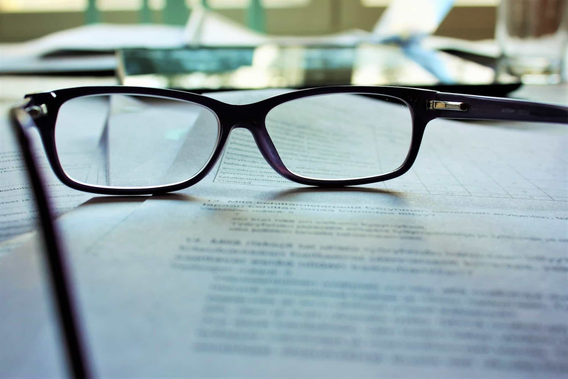 Papers on a desk with black-framed eyeglasses on top