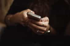 Both of a woman’s hands holding a smartphone while typing on it.