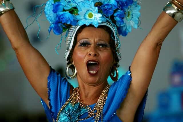 Seorang wanita dengan gaun biru tanpa lengan dan rumit, hiasan kepala bunga menari dan berteriak di Karnaval di Sao Paulo, Brasil.