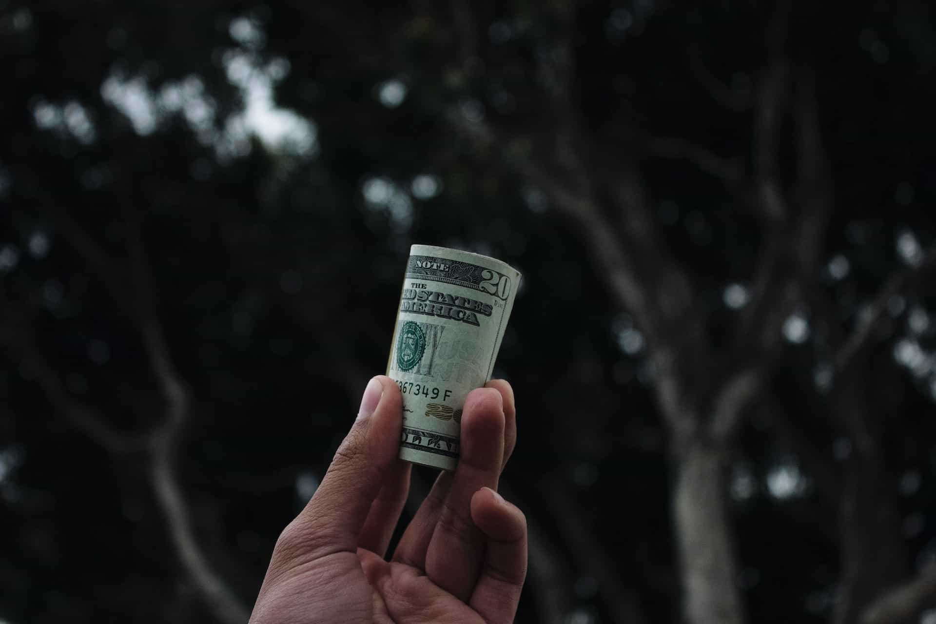 A hand holds up a roll of US money in paper bills.