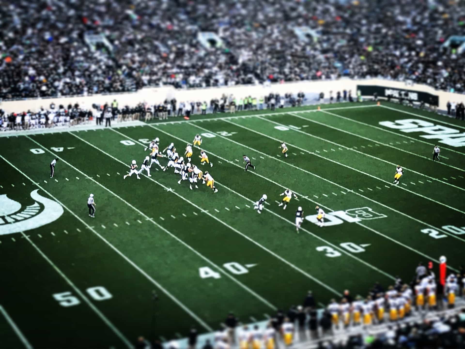 A game of American football underway on an outdoor field in a packed stadium.