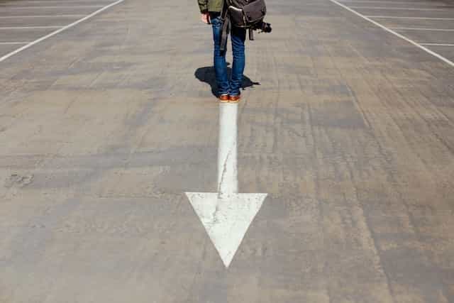 A person standing at the base of a downward pointing arrow painted onto a smooth concrete floor.