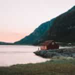 A reddish brown house beside body of water near a mountain.