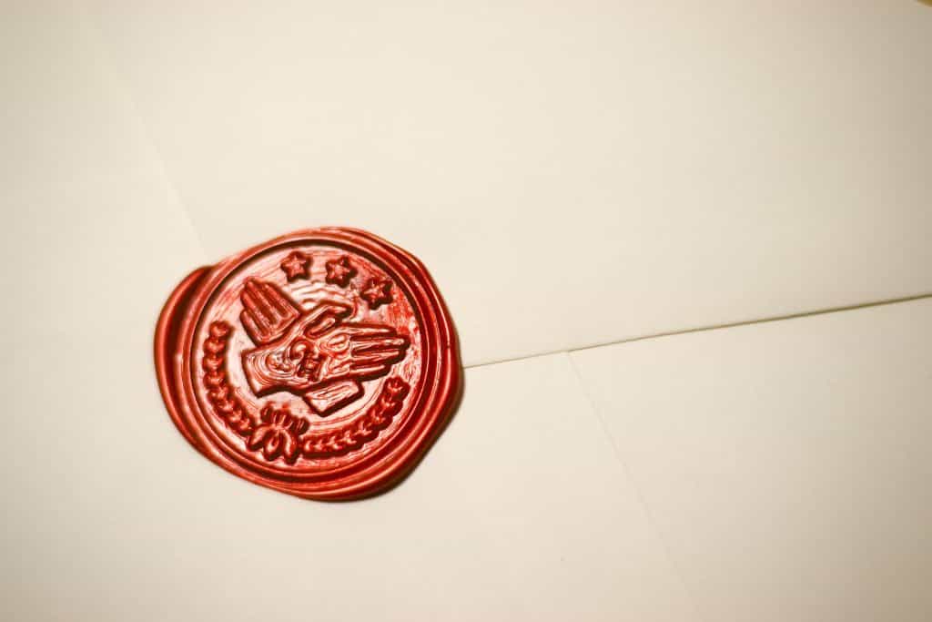 A red wax seal on an envelope depicts a logo with two hands and a wreath.