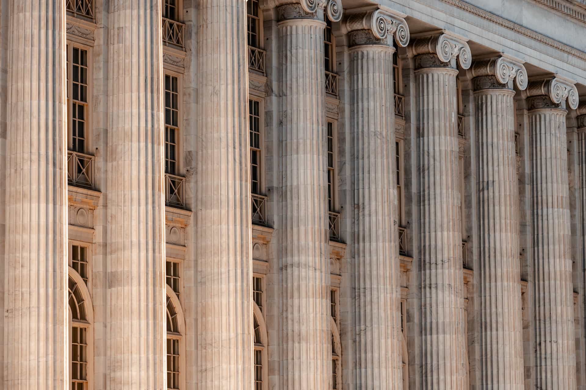 The face of a large building with many columns.