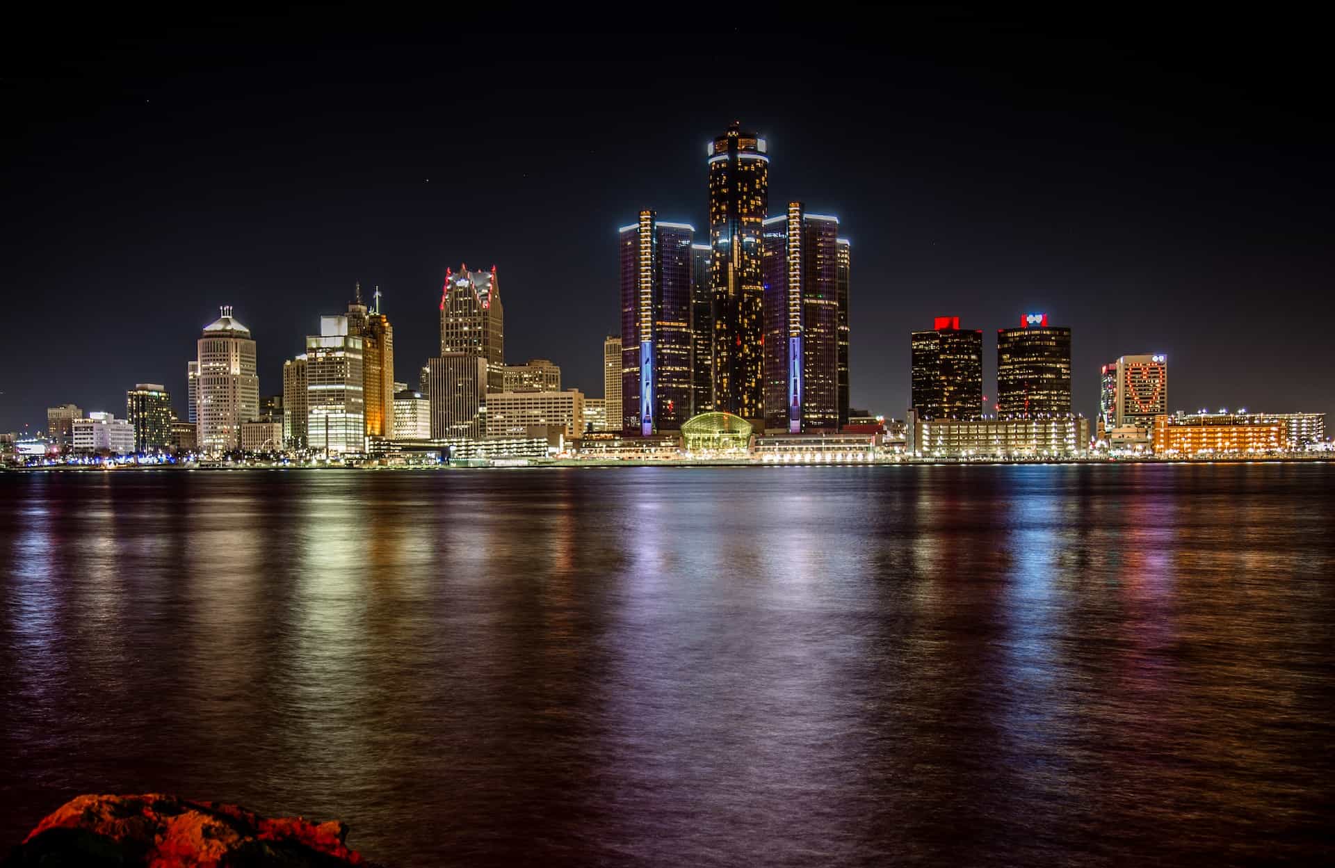 A view of downtown Detroit, Michigan from Lake Michigan, featuring several tall buildings and skyscrapers lighting up the night sky.