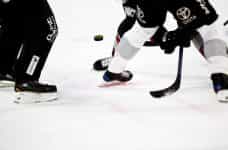 Several hockey players vying for control of the puck on an ice rink during a game of hockey.