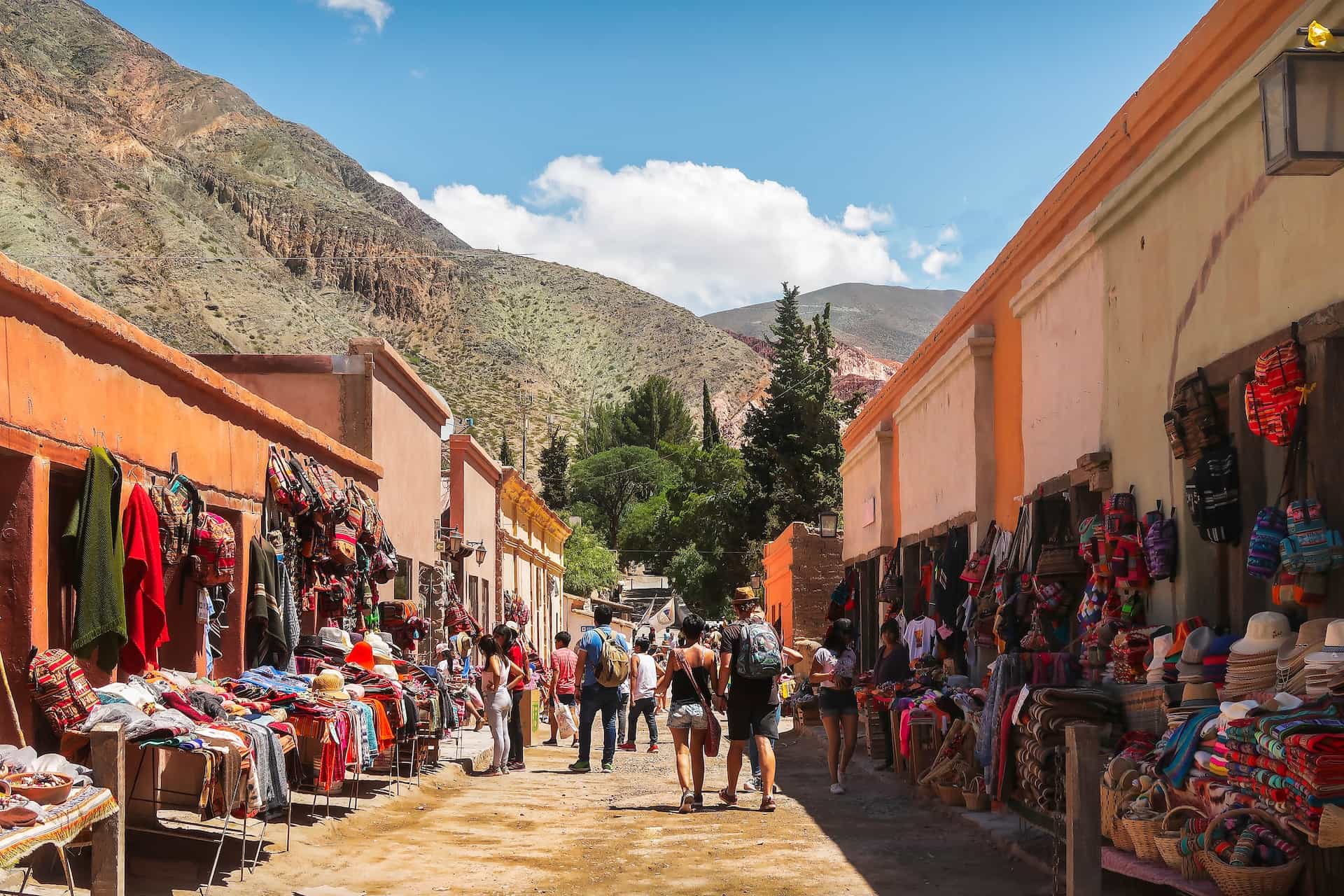 A busy street in Purmamarca, Jujuy, Argentina, with street vendors and red buildings.
